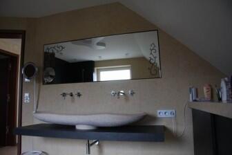 Badezimmer mit handgemeißeltem Waschbecken und einem hinterleuchteten Spiegel